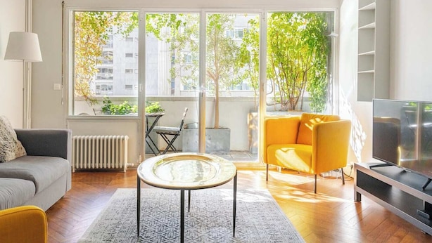 Una sala de estar moderna con un sofá, un sillón amarillo, una mesa de centro de vidrio y un televisor.