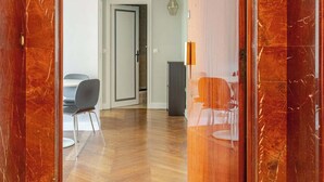 Un pasillo con piso de madera y pared de mármol. Hay una puerta que da a otra habitación.