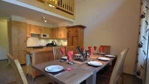 Ein Essbereich mit einem Holztisch, gedeckt für vier Personen, eine Küche mit Holzschränken und eine Treppe, die zu einer oberen Ebene führt.