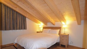 Ein Schlafzimmer mit Holzboden, einem Bett mit weißer Bettwäsche, zwei Nachttischen mit Lampen und einem Fenster mit Vorhängen.