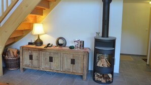 Eine Treppe mit hölzernen Geländern, ein Holzschrank mit Lampe sowie ein schwarzer Holzofen mit Holzscheiten.