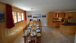 Un comedor con una mesa de madera preparada para el desayuno, armarios de madera y una zona de cocina con microondas y fregadero.