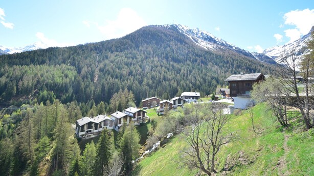 Un pueblo de montaña con edificios de estilo chalete, rodeado de densos bosques y picos nevados.