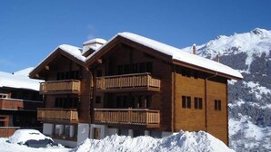 Eine Holzhütte mit Balkon, vor einer verschneiten Berglandschaft.