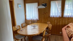 Ein Holztisch mit sechs Stühlen, eine hängende Leuchte und ein Fenster mit Spitzenvorhängen.