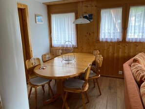 Ein Holztisch mit sechs Stühlen, eine hängende Leuchte und ein Fenster mit Spitzenvorhängen.