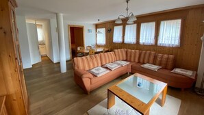 Ein geräumiges Wohnzimmer mit einer großen, L-förmigen Couch, einem Glastisch und Holzböden.