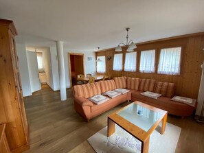 Ein geräumiges Wohnzimmer mit einer großen, L-förmigen Couch, einem Glastisch und Holzböden.