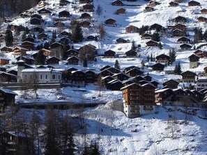Ein verschneites Dorf mit traditionellen Holzhäusern, einige mit Balkonen, und einigen größeren Gebäuden.
