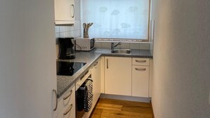 Eine kompakte Küche mit weißen Schränken, einer Arbeitsplatte mit Kaffeemaschine, Mikrowelle und Spüle.
