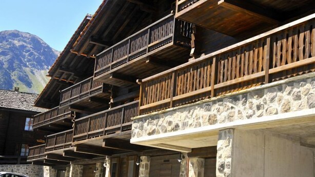 Ein traditionelles Chalet mit Holzbalkonen und Steinwänden, vor einer Bergkulisse gelegen.