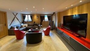 Ein modernes Wohnzimmer mit einem großen Flachbildfernseher, einem Ecksofa und roten und schwarzen Sesseln.