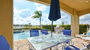 An outdoor patio with a table set for dining, chairs, and a view of a swimming pool.