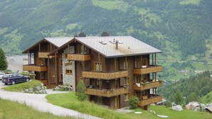 Ein mehrstöckiges Holzchalet mit Balkonen in einer gebirgigen Landschaft.