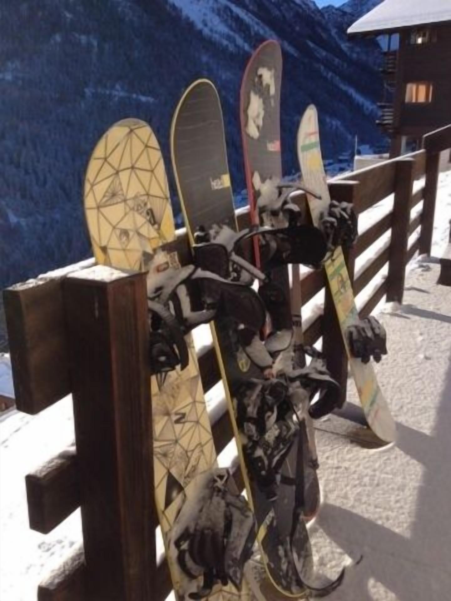 A row of snowboards leaning against a wooden fence on a snowy slope.