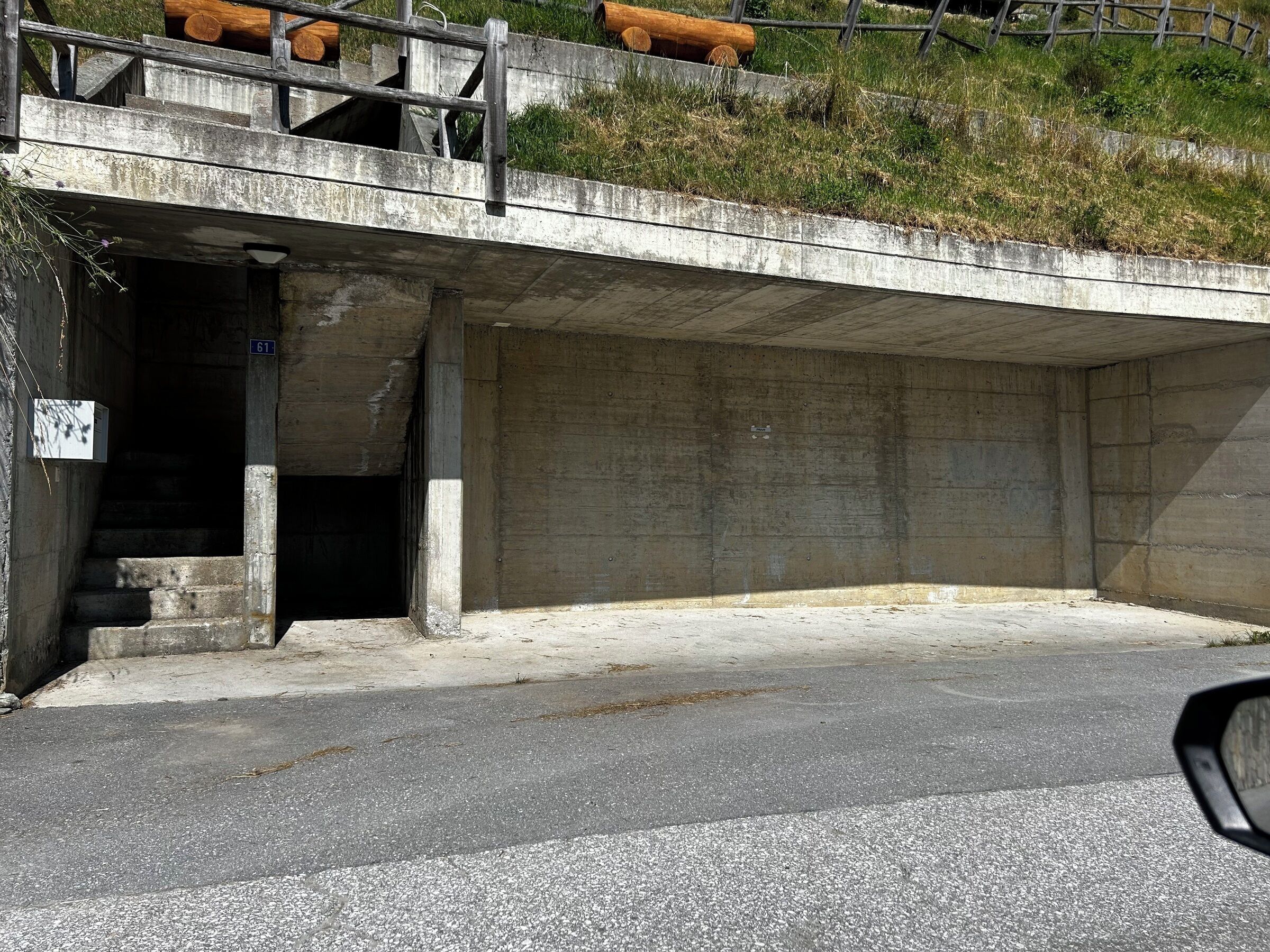 A concrete structure with a staircase leading into a covered area, a metal railing, and a road in front.