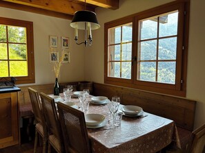 Ein Esszimmer mit Holztisch, gedeckt für vier Personen, großen Fenstern mit Blick auf die Landschaft und einer Chandelier.
