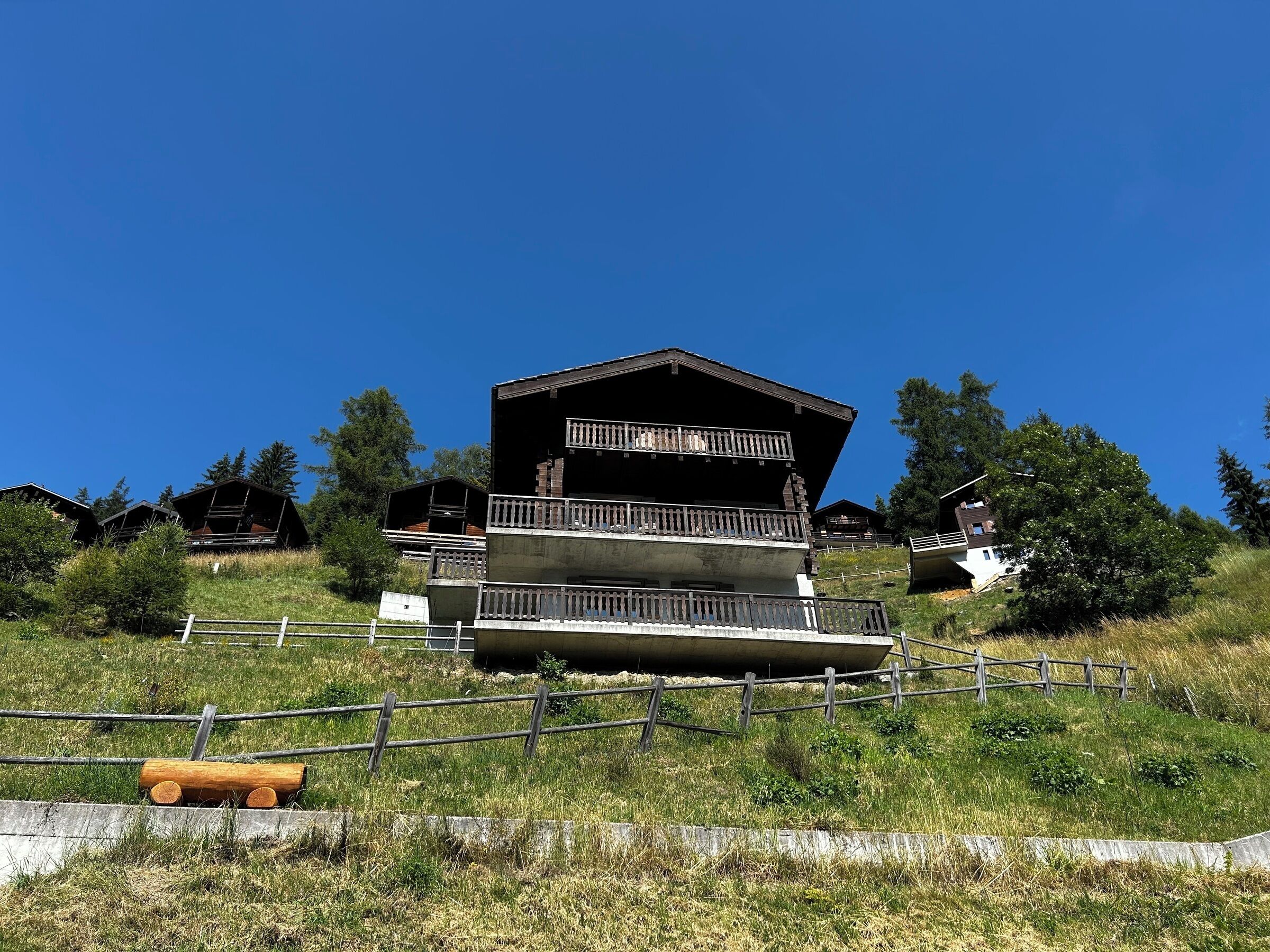 Ein Chalet mit Balkon im zweiten Stock, umgeben von Grünpflanzen und ähnlichen Gebäuden.