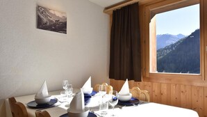 Mesa de comedor con vajilla blanca y azul, una ventana con vista a la montaña, paneles de madera y un cuadro en la pared.