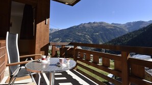 Un balcón de madera con una mesa redonda y sillas, con vistas a un paisaje montañoso.