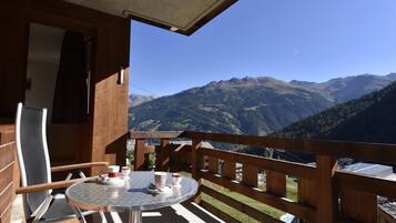 Ein Holzbalkon mit einem runden Tisch und Stühlen, mit Blick auf eine gebirgige Landschaft.