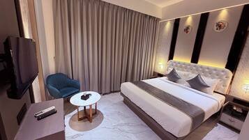 Quarto de hotel moderno com uma cama grande, televisão, uma cadeira e uma mesa pequena.