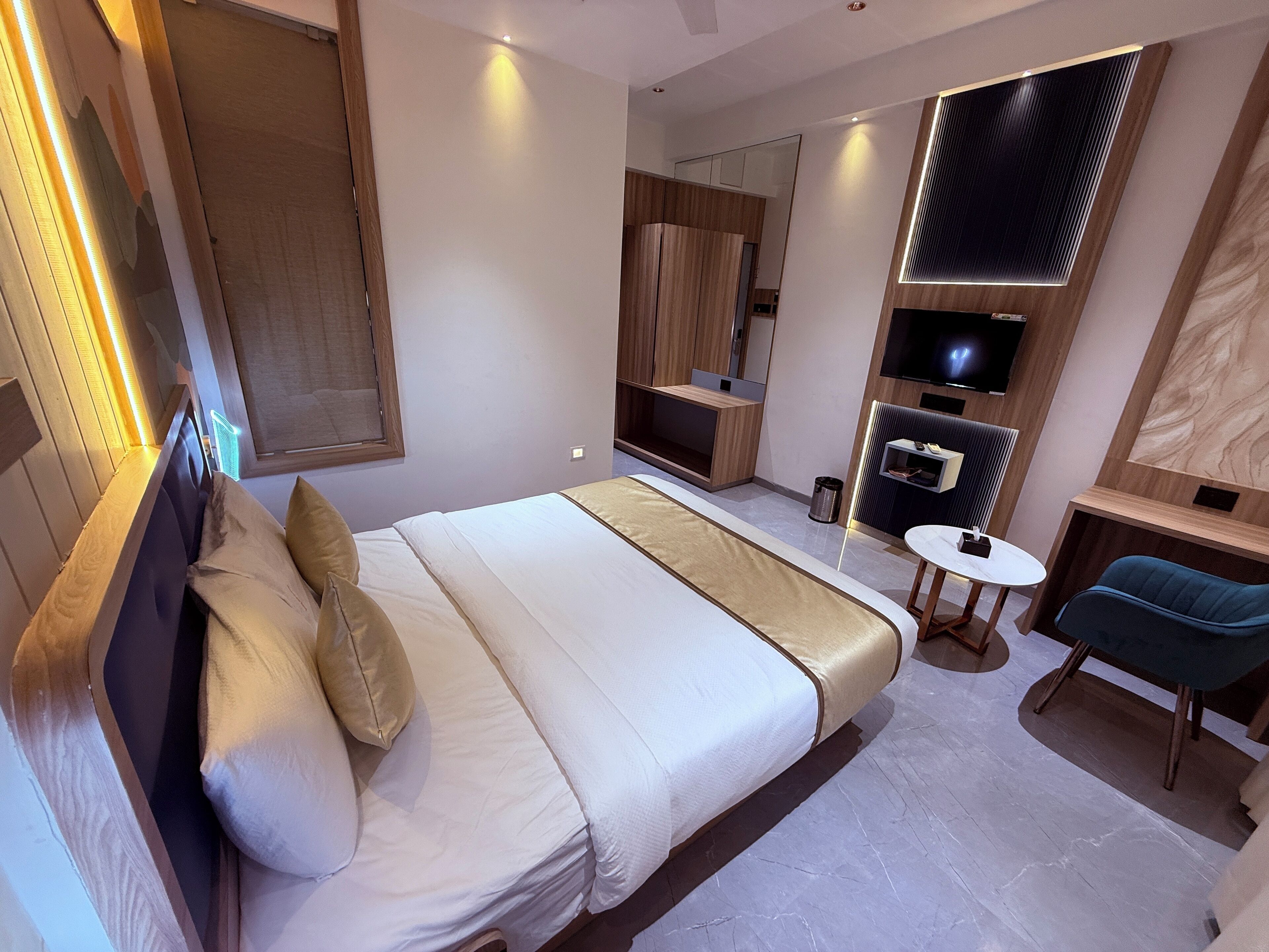 Une chambre d’hôtel moderne avec un grand lit, une petite table, une chaise, un téléviseur et des étagères intégrées.