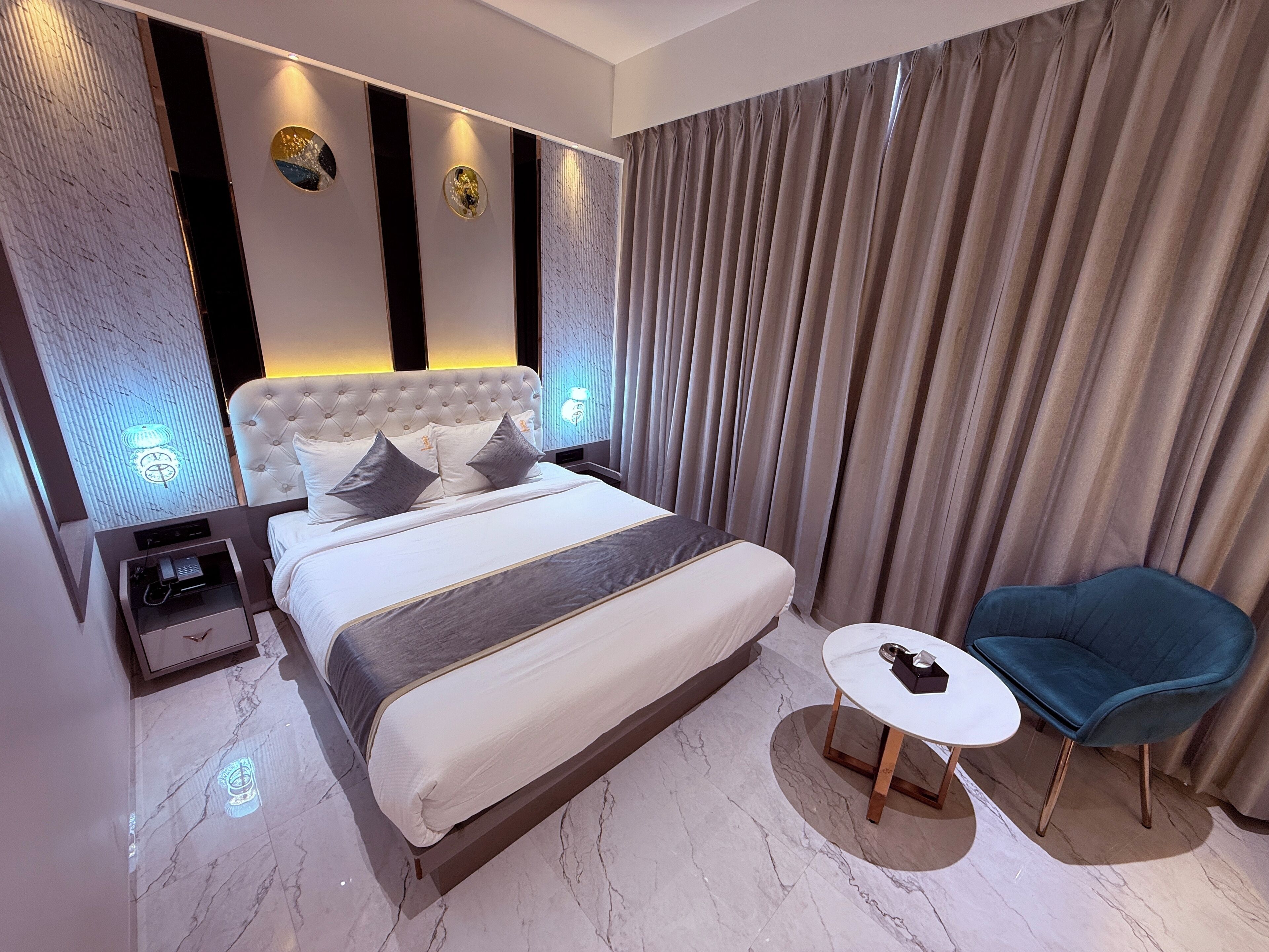 Une chambre moderne avec un grand lit, une table de chevet, une petite table ronde et une chaise bleue.