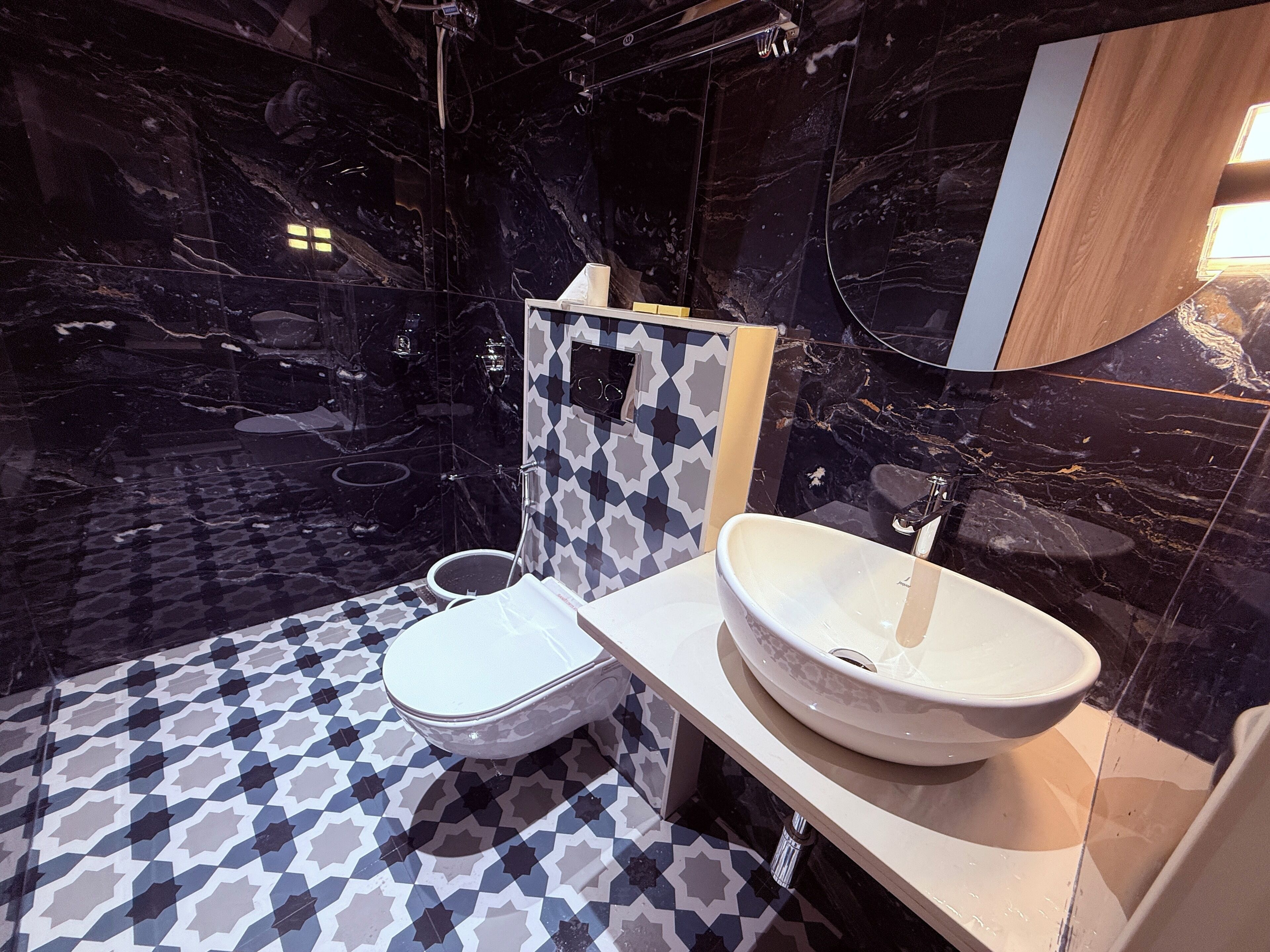 Een badkamer met een vloer van zwart marmer, een wit toilet, een groot wit wastafel en een douchegedeelte.