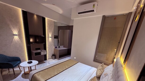 Ein modernes Hotelzimmer mit einem großen Bett, einer Sitzecke mit einem Sessel und einem kleinen Tisch, einem Frisiertisch mit Spiegel sowie einer Klimaanlage an der Wand.