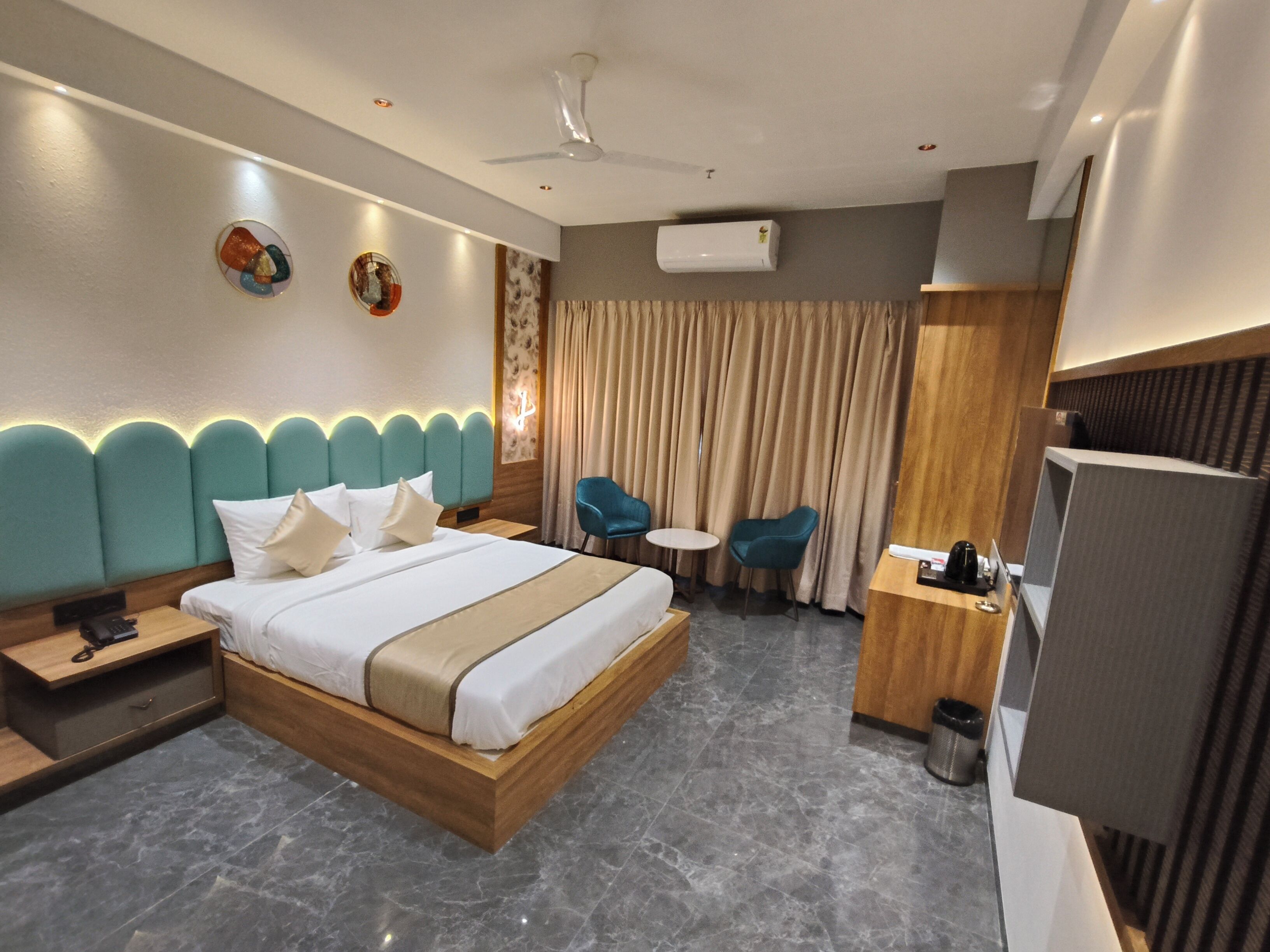 Ein modernes Hotelzimmer mit einem großen Bett, einem Schreibtisch, einem Sessel, einem kleinen Tisch und einer Klimaanlage.