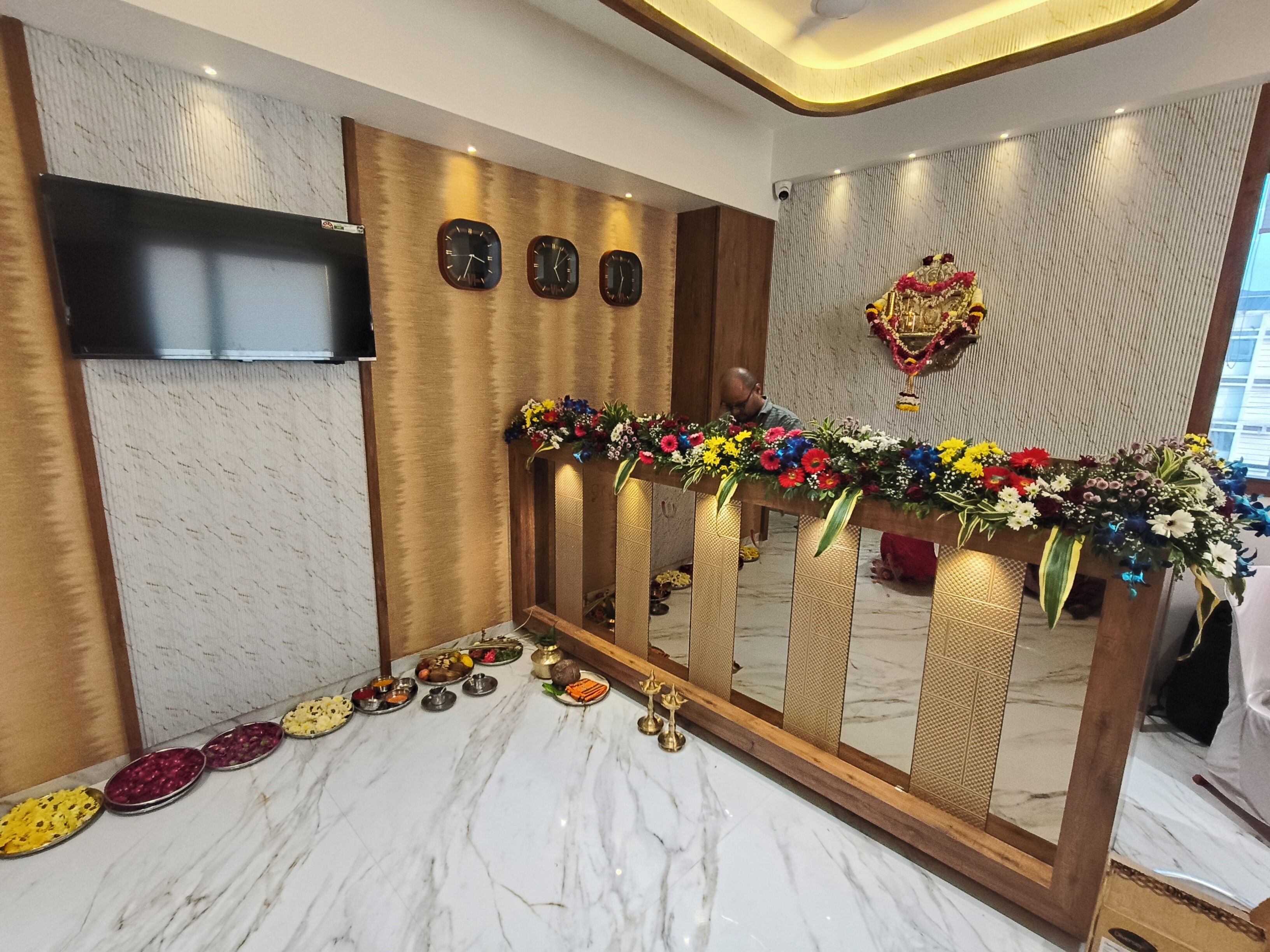 Un espace d’accueil doté d’un sol en marbre, d’un téléviseur fixé au mur, de trois horloges et d’un arrangement floral.