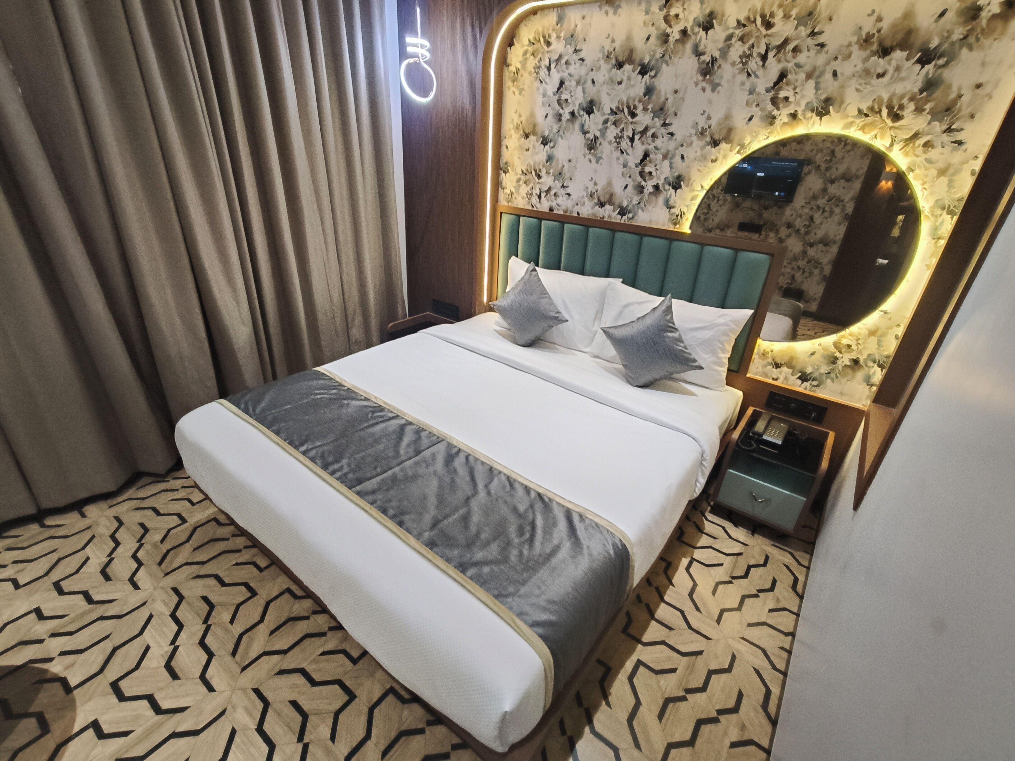 Ein Hotelzimmer mit einem Bett, einem Nachttisch, einem Spiegel und einer Wand mit Blumenmuster.
