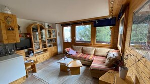 Et hyggeligt værelse i sommerhusstil med træpaneler, en sofa, et sofabord og et tekøkken med skabe og vask.