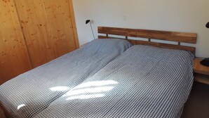 A bedroom with a wooden headboard, a checkered bedspread, and a wooden door. - 2 room apartment for 2-4 persons : Living room with sofa-bed and 1 pull-down bed - kitchen with dish (Grimentz)