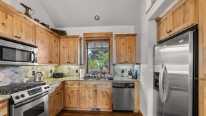 Une cuisine moderne avec des meubles en bois, des appareils électroménagers en acier inoxydable, un pare-feu en pierre et une fenêtre donnant sur un paysage verdoyant.