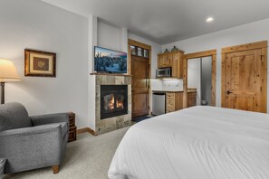 A bedroom with a fireplace, a bed, a sofa, a television, and wooden cabinets.