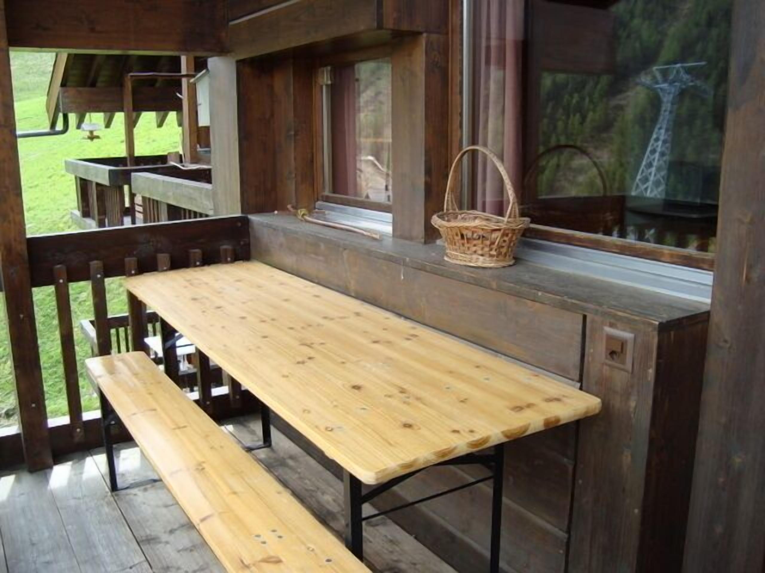 A wooden picnic table and bench on a porch with a view of a grassy area and a giraffe in the background.