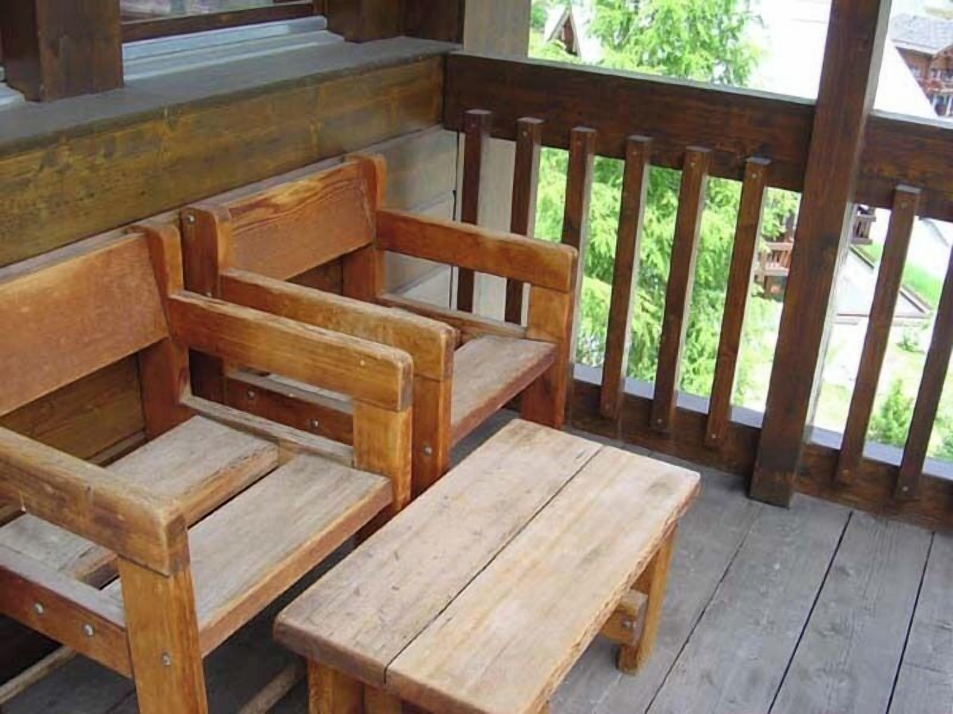 A wooden bench with a backrest and a small table, placed on a wooden deck with a railing.