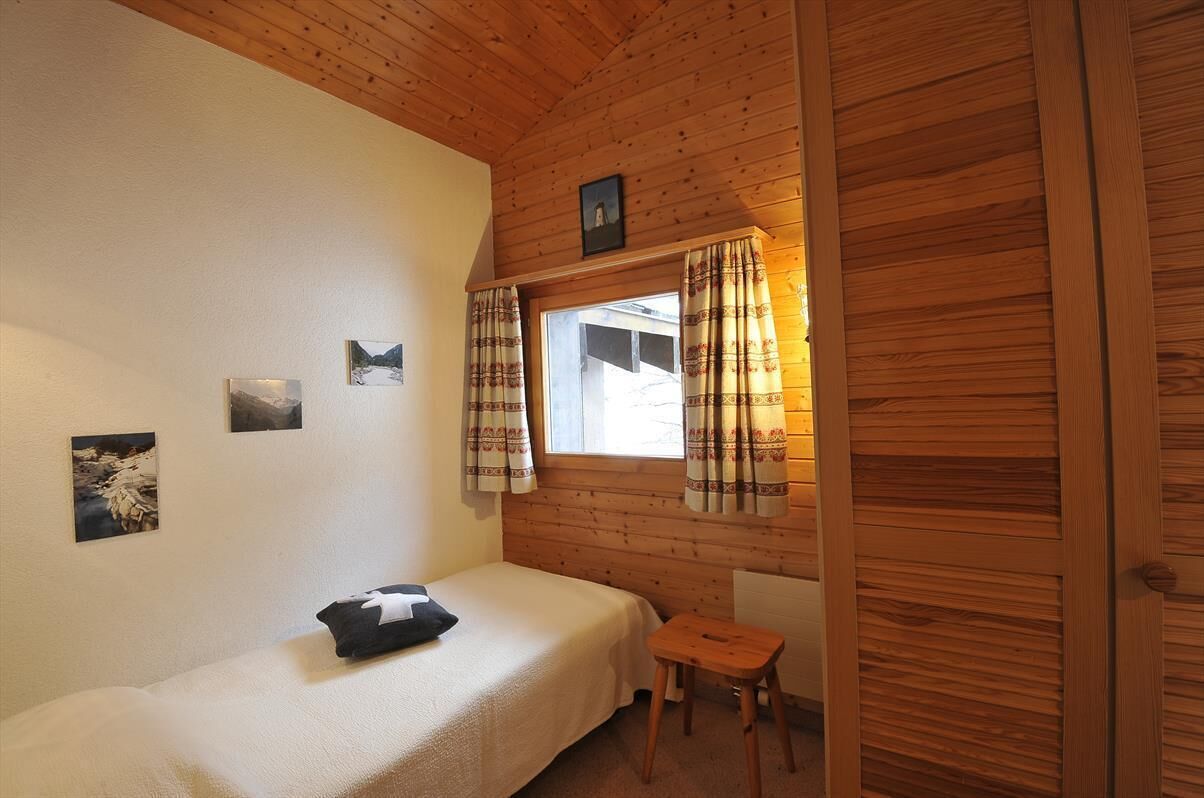 Ein kleiner, gemütlicher Raum mit Holzwänden, einem Einzelbett, einem kleinen Tisch und einem Fenster mit Vorhängen.