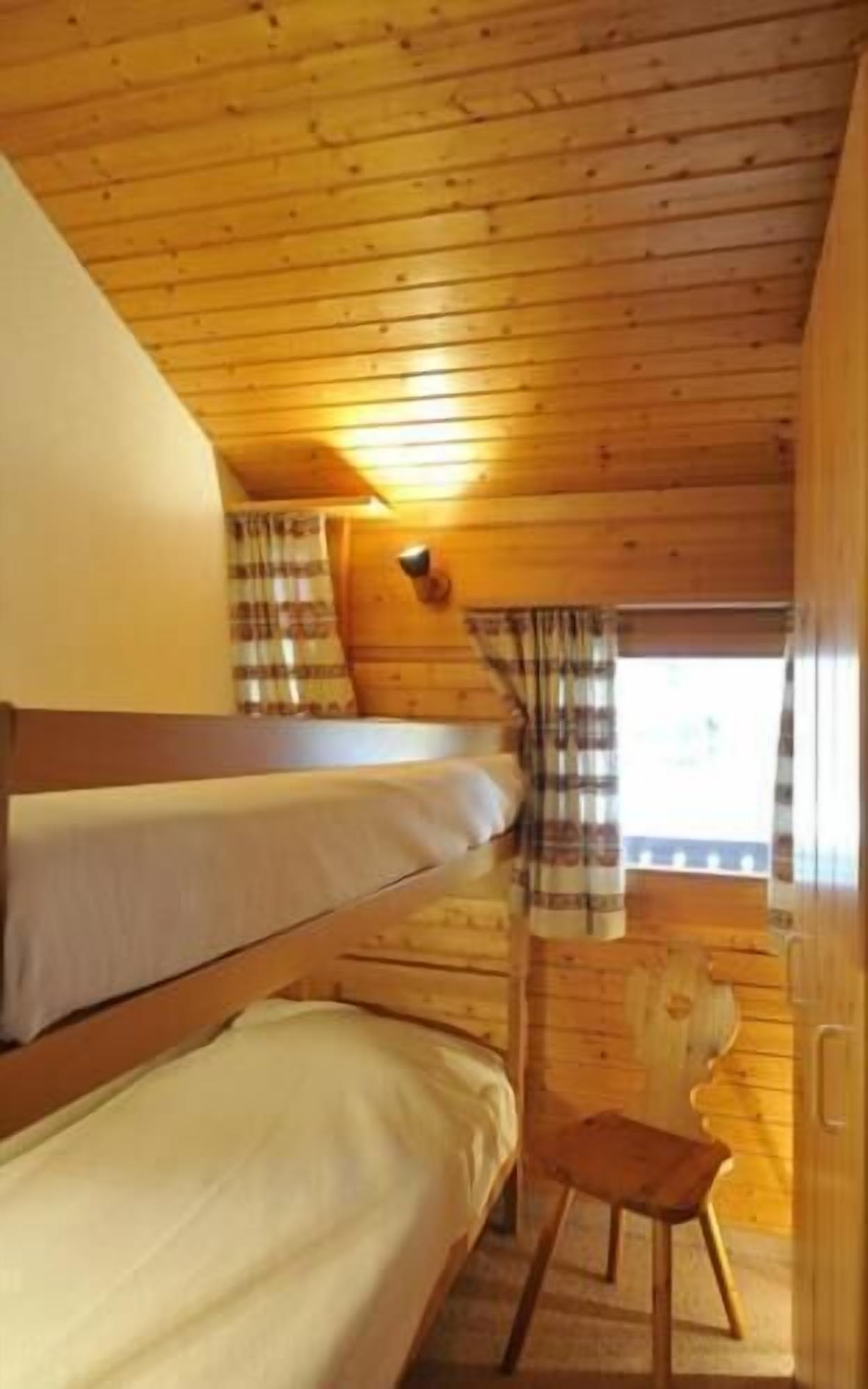 Una cabaña con paredes de madera y techo inclinado. Hay dos literas y una pequeña silla de madera.