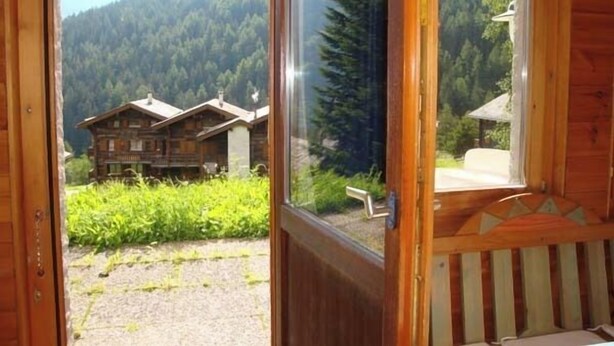 Uma cabana de madeira com uma janela grande que oferece vista para uma área montanhosa coberta por floresta.