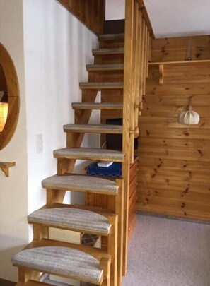 A wooden staircase with a circular mirror on the left and a wooden wall with a hanging object on the right. - Comfortable 2-room duplex apartment for 2 persons : Living room - kitchenette - 1 room with 2 beds - (Grimentz)