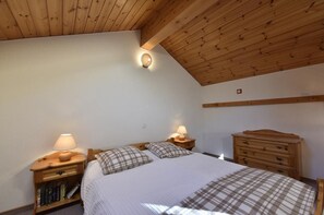 A bedroom with a wooden ceiling, a bed with plaid bedding, two bedside tables with lamps, a wooden dresser, and a bookshelf. - Comfortable 2-room duplex apartment for 2 persons : Living room - kitchenette - 1 room with 2 beds - (Grimentz)