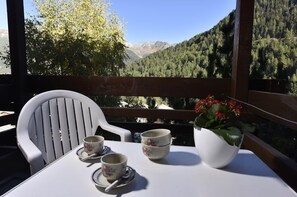 Een balkon met een tafel, twee stoelen en een bloempot.