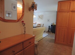 Ein Zimmer mit einem hölzernen Schminktisch, einem Spiegel, einer Vase mit Blumen, einem Bett, einem Holzschrank und einem Essbereich im Hintergrund.