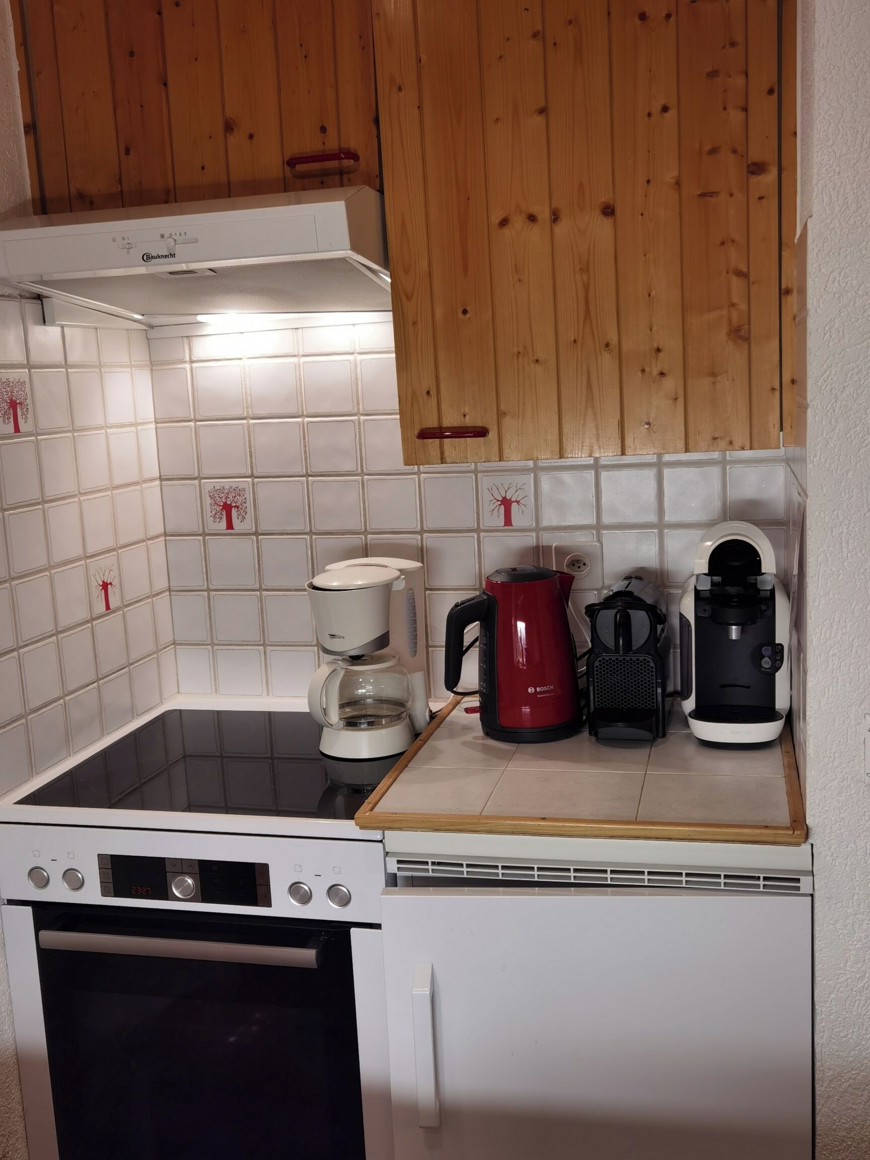 Une cuisine compacte équipée d’une machine à café Bosch, d’une cafetière rouge de la marque Bosch et d’une autre machine à café blanche, le tout posé sur le plan de travail.