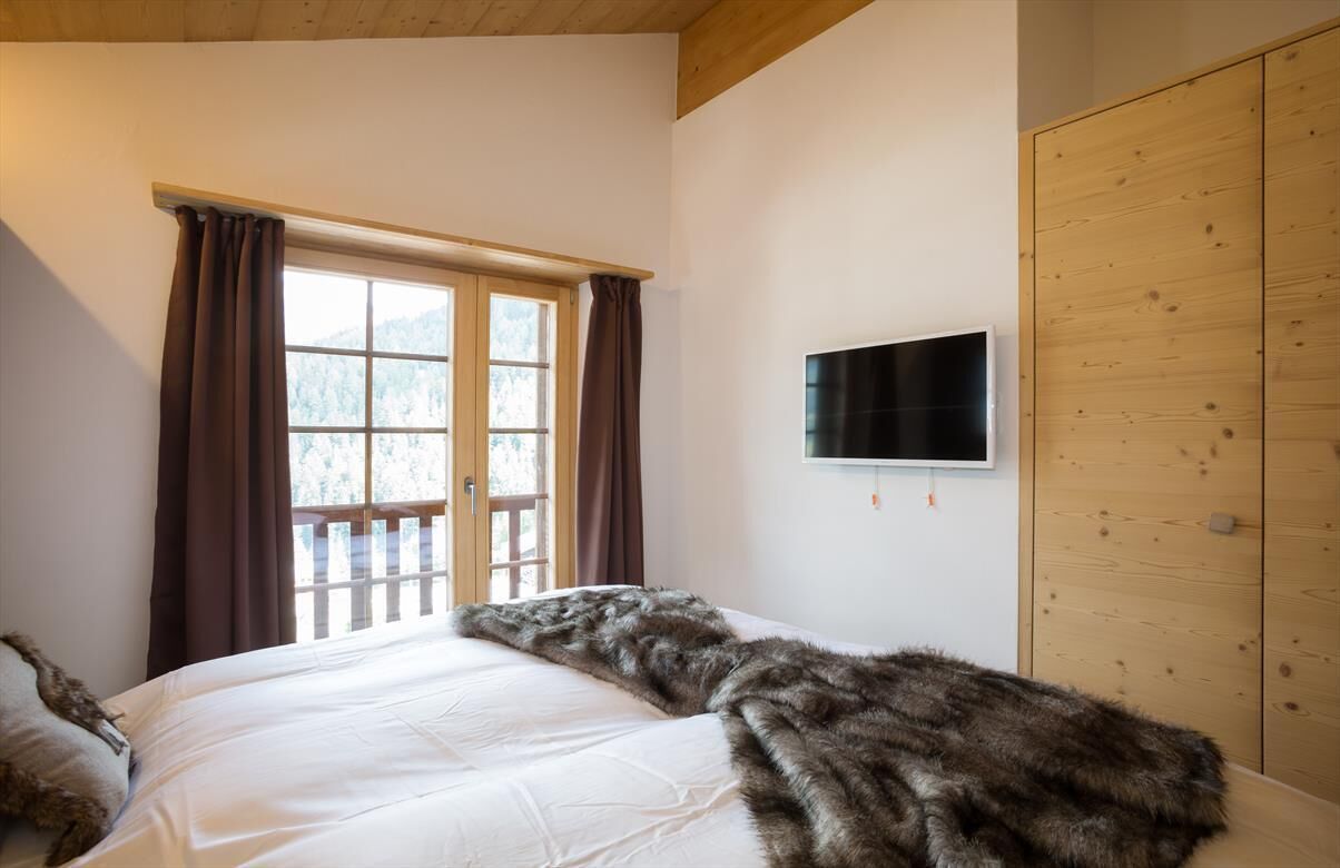Ein Schlafzimmer mit Bett, einem Vorhangfenster, einem an der Wand befestigten Fernseher und einem Holzschrank.