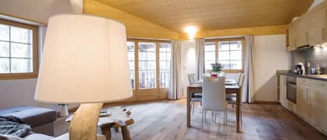 A spacious room with a wooden ceiling, a dining area with a table and chairs, and a kitchen area with cabinets and appliances.