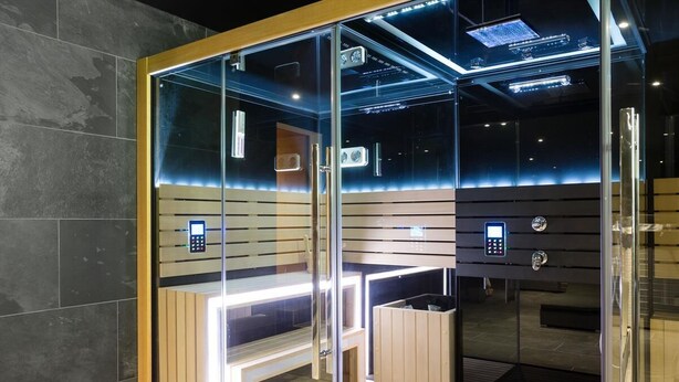Een moderne, afgesloten sauna met glazen wanden, houten banken en ingebouwde verlichting.